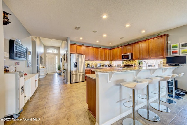 kitchen with a peninsula, appliances with stainless steel finishes, brown cabinetry, and visible vents