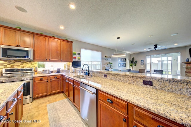 kitchen with light stone counters, light tile patterned floors, appliances with stainless steel finishes, brown cabinetry, and a sink