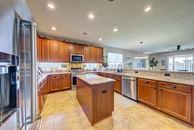 kitchen with a kitchen island, a sink, appliances with stainless steel finishes, light stone countertops, and brown cabinetry