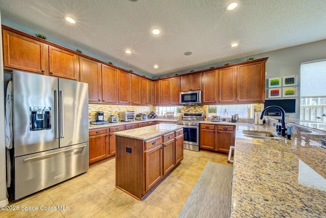 kitchen with light stone counters, a center island, stainless steel appliances, tasteful backsplash, and a sink