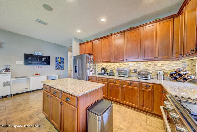 kitchen with light stone counters, light tile patterned floors, high end fridge, backsplash, and range