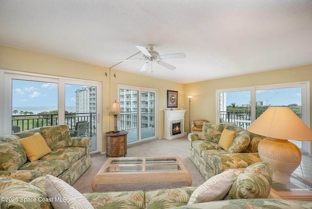 living room with light carpet, a lit fireplace, and a ceiling fan