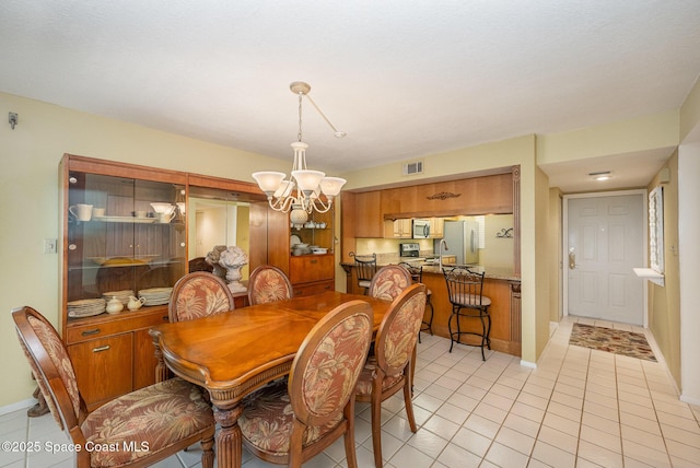 dining space with light tile patterned floors, baseboards, visible vents, and a chandelier