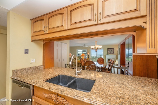 kitchen with light stone counters, a fireplace, a sink, open floor plan, and stainless steel dishwasher