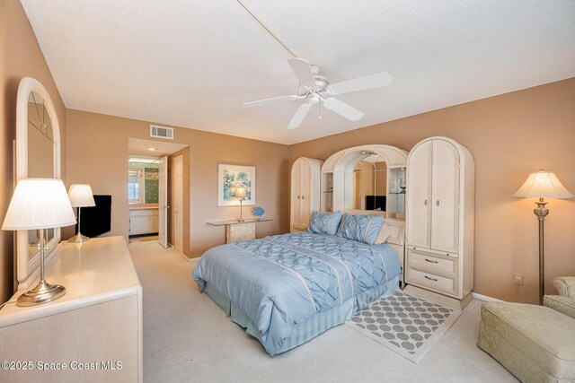 bedroom with a textured ceiling, arched walkways, light colored carpet, a ceiling fan, and visible vents