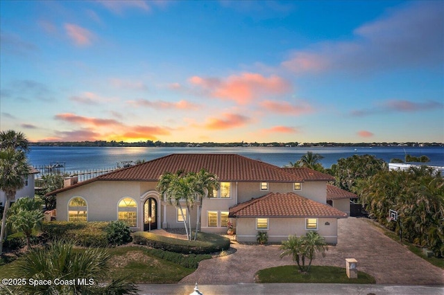 mediterranean / spanish house with a tile roof, stucco siding, a water view, and curved driveway