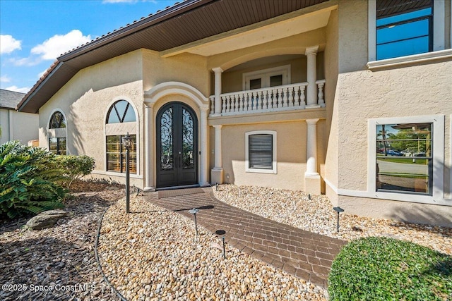 view of exterior entry featuring stucco siding, french doors, and a balcony