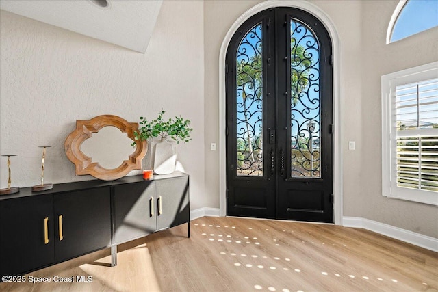 entrance foyer with french doors, arched walkways, baseboards, and wood finished floors