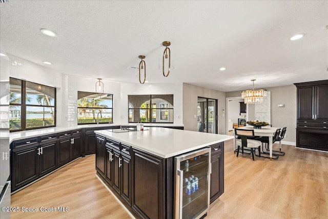 kitchen featuring light wood-style flooring, a chandelier, beverage cooler, and light countertops