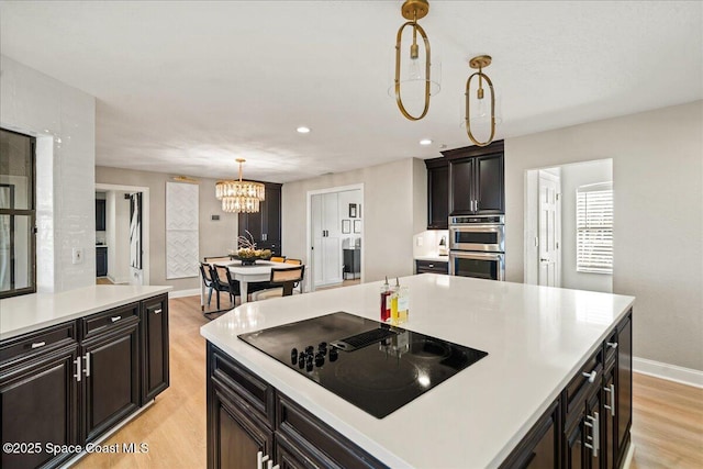 kitchen with light wood finished floors, light countertops, decorative light fixtures, black electric cooktop, and a chandelier