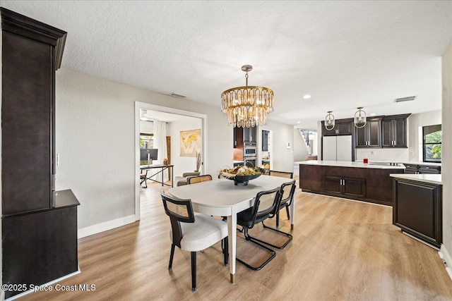 dining room with visible vents, baseboards, a chandelier, light wood-style flooring, and a textured ceiling