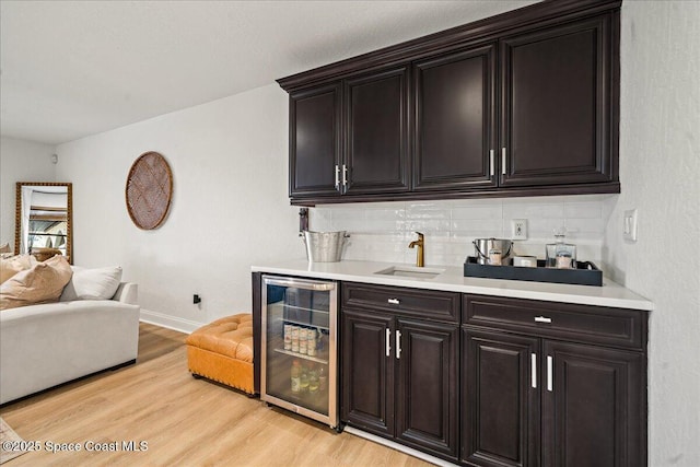 bar featuring backsplash, baseboards, beverage cooler, light wood-style flooring, and a sink