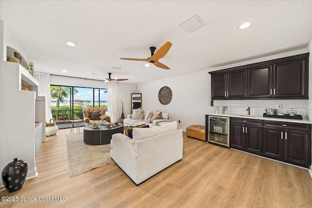 living room with beverage cooler, visible vents, recessed lighting, indoor wet bar, and light wood-type flooring