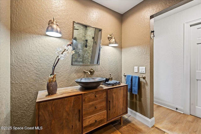 full bathroom with walk in shower, vanity, baseboards, and a textured wall