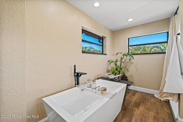 bathroom featuring wood finished floors, baseboards, a soaking tub, recessed lighting, and a textured wall