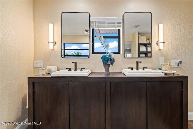 full bathroom with a sink, visible vents, double vanity, and a textured wall