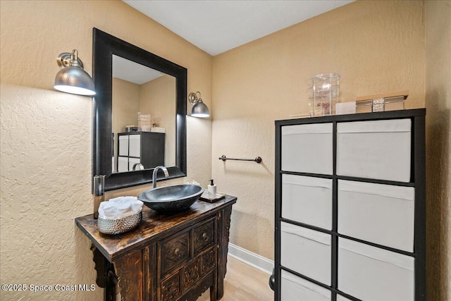 bathroom with vanity, wood finished floors, baseboards, and a textured wall