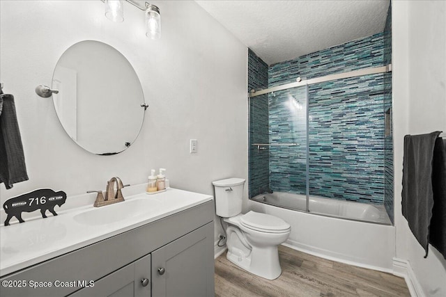 full bathroom with toilet, a textured ceiling, wood finished floors, bath / shower combo with glass door, and vanity