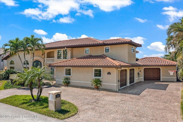 mediterranean / spanish home featuring a tiled roof, an attached garage, driveway, and stucco siding