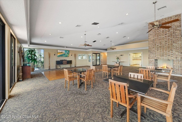 carpeted dining room featuring a fireplace, vaulted ceiling, a ceiling fan, and visible vents