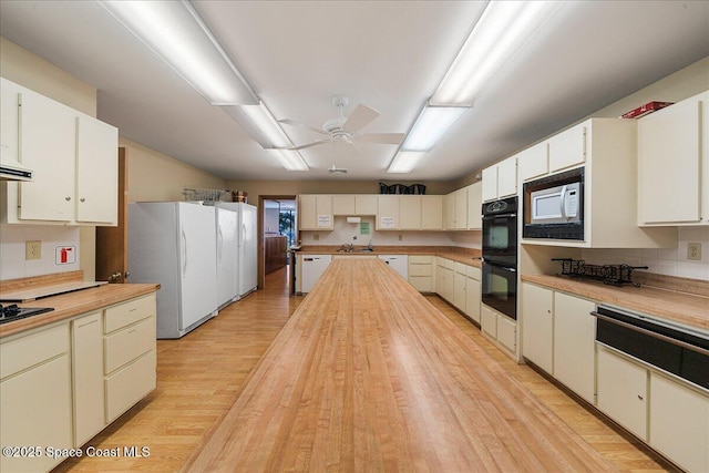 kitchen with a ceiling fan, a sink, butcher block countertops, black appliances, and light wood-style floors