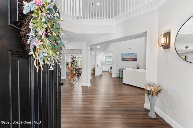 entrance foyer with a textured wall, wood finished floors, a towering ceiling, and baseboards