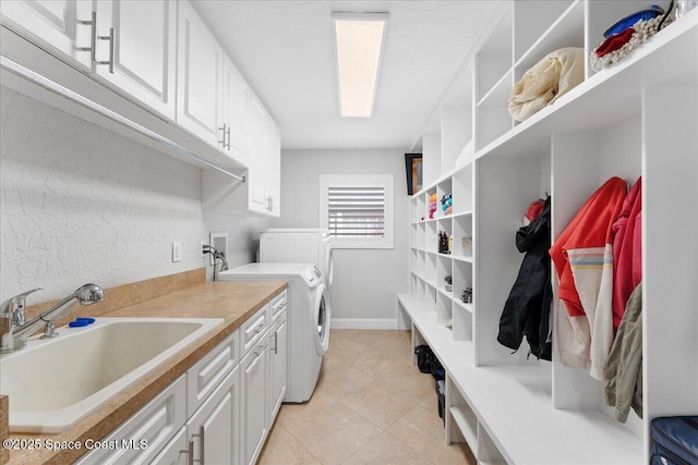 laundry room featuring light tile patterned floors, a sink, baseboards, cabinet space, and washer and clothes dryer