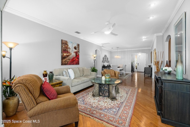 living room featuring arched walkways, light wood finished floors, visible vents, and crown molding