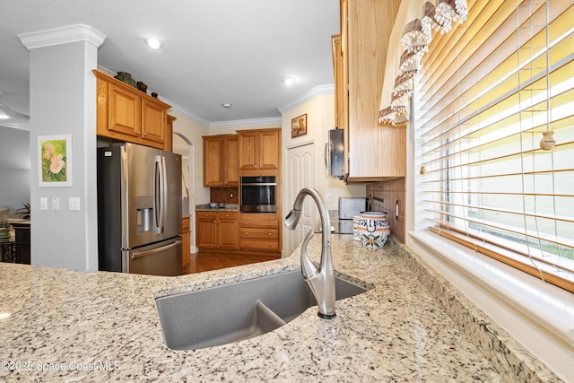 kitchen featuring light stone counters, recessed lighting, stainless steel appliances, a sink, and ornamental molding