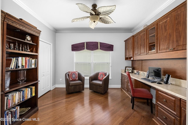 office space with baseboards, dark wood-style floors, ceiling fan, crown molding, and built in desk