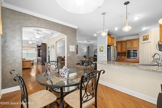 dining area featuring arched walkways, visible vents, light wood-style floors, ornamental molding, and ceiling fan