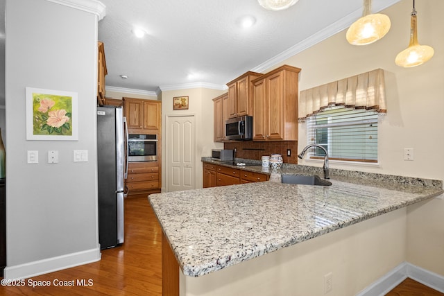 kitchen featuring appliances with stainless steel finishes, wood finished floors, a peninsula, light stone countertops, and a sink