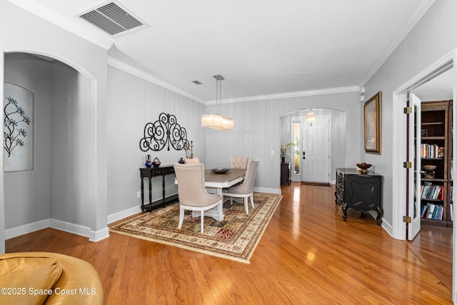 dining room featuring arched walkways, light wood-style flooring, visible vents, baseboards, and ornamental molding