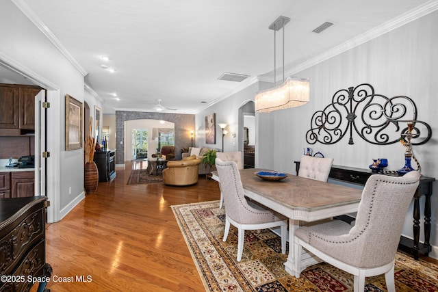 dining room featuring arched walkways, visible vents, baseboards, ornamental molding, and light wood finished floors