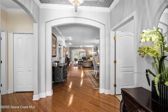 corridor with arched walkways, ornamental molding, and wood finished floors