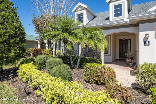 entrance to property featuring a shingled roof and stucco siding