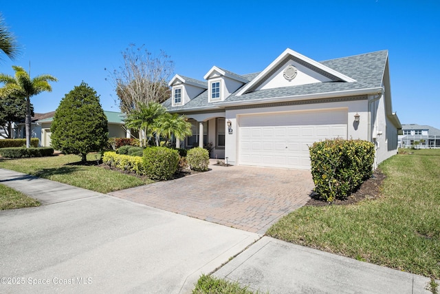 view of front of property with a front yard, decorative driveway, an attached garage, and stucco siding