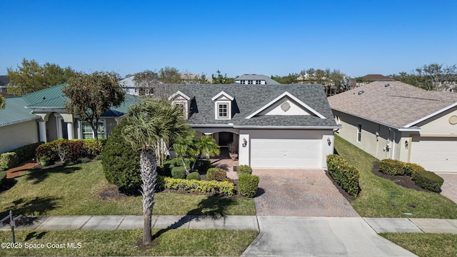 view of front of property with decorative driveway, stucco siding, a shingled roof, an attached garage, and a front lawn