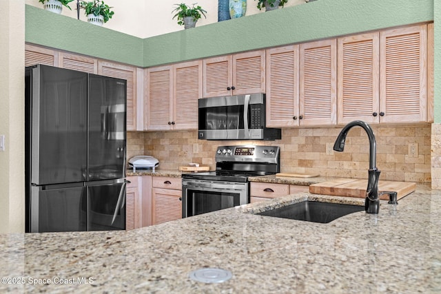 kitchen featuring stainless steel appliances, tasteful backsplash, a sink, and light stone countertops