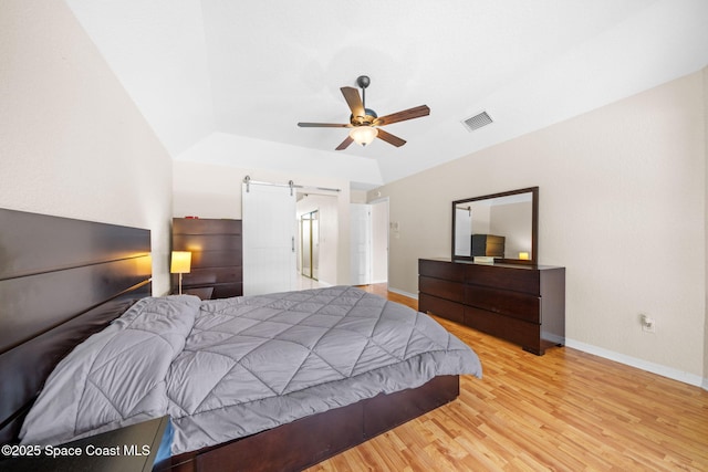 bedroom with a barn door, baseboards, visible vents, a ceiling fan, and wood finished floors