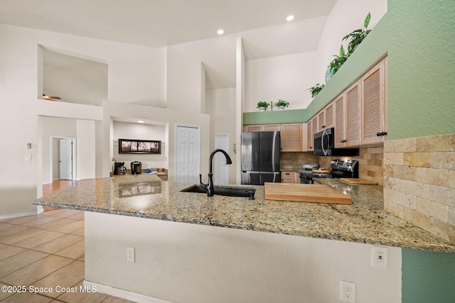 kitchen featuring decorative backsplash, appliances with stainless steel finishes, light stone counters, a peninsula, and a sink