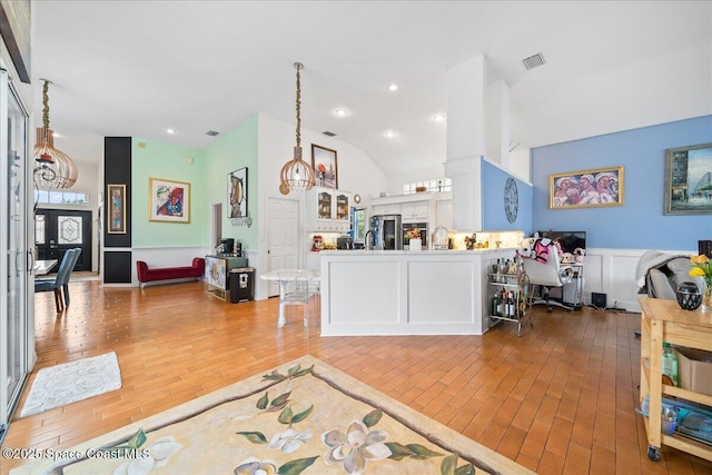 530 Carmel Dr, Melbourne, FL 32940 - interior space featuring light wood finished floors, visible vents, vaulted ceiling, a decorative wall, and wainscoting