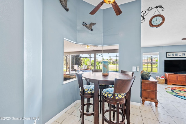 tiled dining space with baseboards, a high ceiling, ceiling fan, and a sunroom