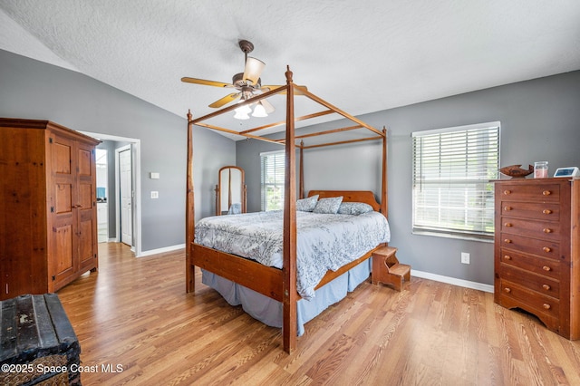 bedroom featuring ceiling fan, baseboards, vaulted ceiling, light wood-style flooring, and a textured ceiling