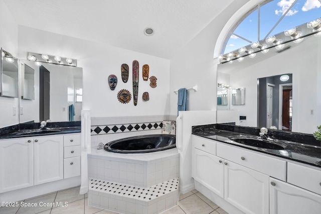 full bath with tile patterned floors, two vanities, a garden tub, and a sink