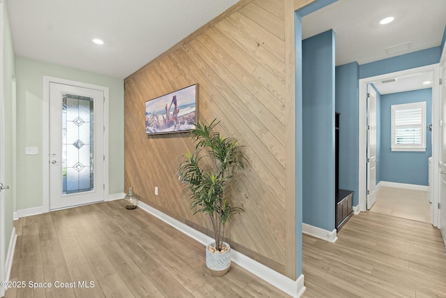 foyer featuring baseboards, an accent wall, light wood finished floors, and wooden walls