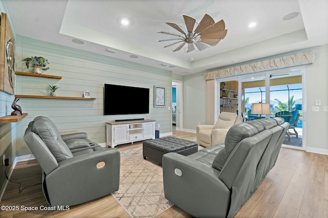 living room with light wood-style floors, baseboards, a tray ceiling, and wood walls