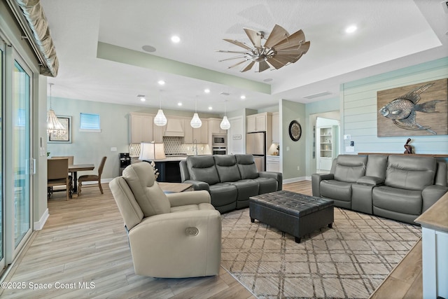 living area featuring light wood-style flooring, a tray ceiling, baseboards, and recessed lighting