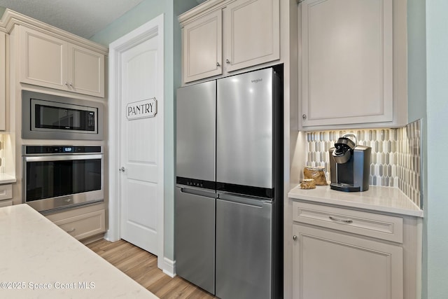 kitchen with light wood-type flooring, backsplash, stainless steel appliances, and light countertops