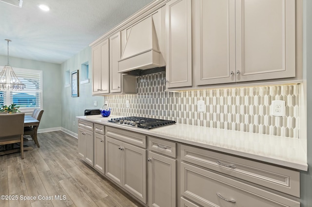 kitchen featuring stainless steel gas cooktop, light wood finished floors, custom exhaust hood, light countertops, and decorative backsplash